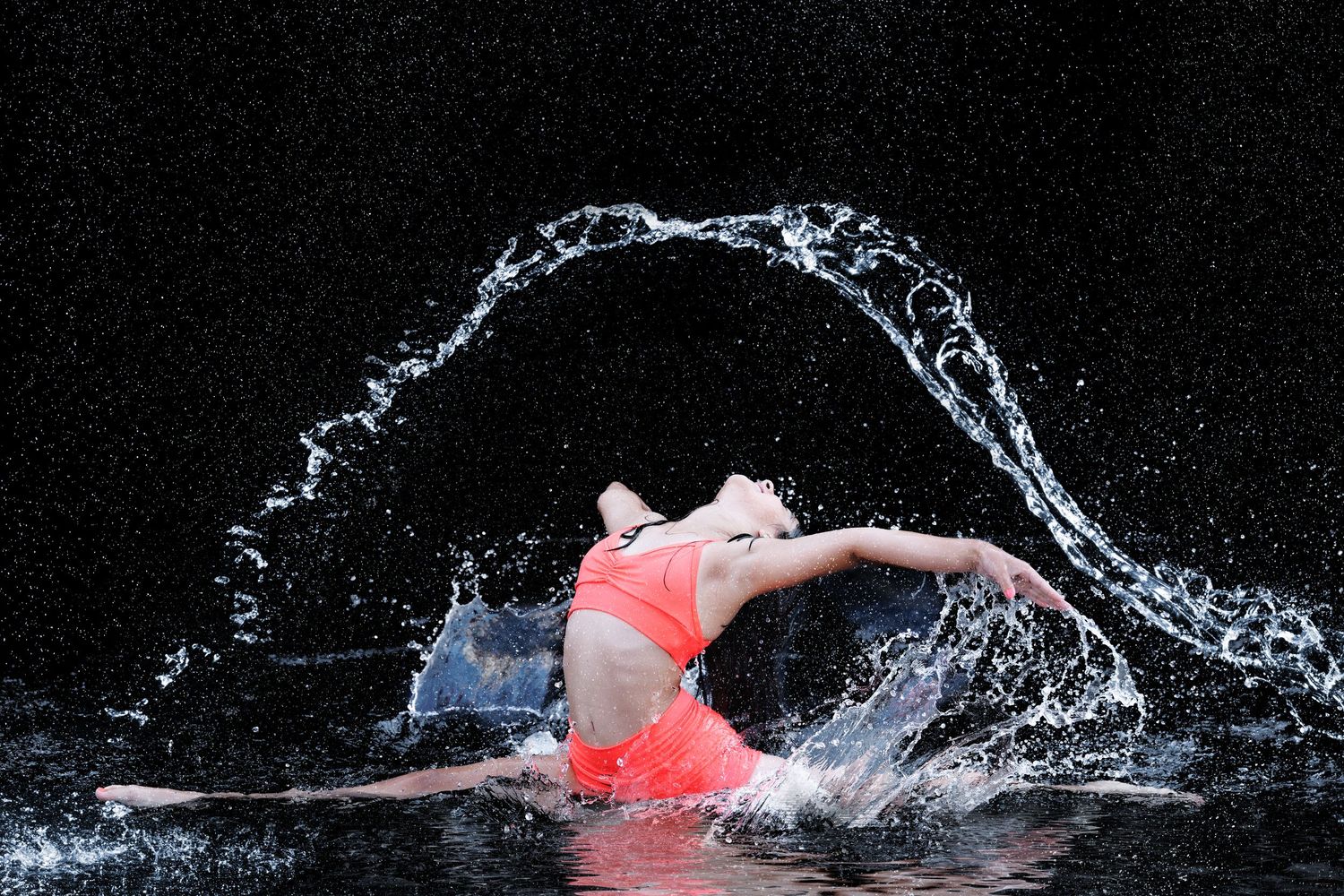 A woman in a red bikini performs a dramatic water splash against a dark background.