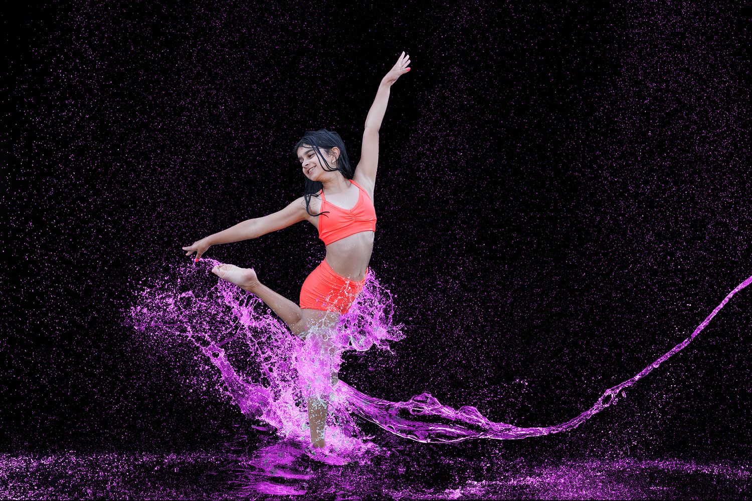 Dancer leaping through vibrant purple water splashes against a dark background, wearing bright orange athletic wear.