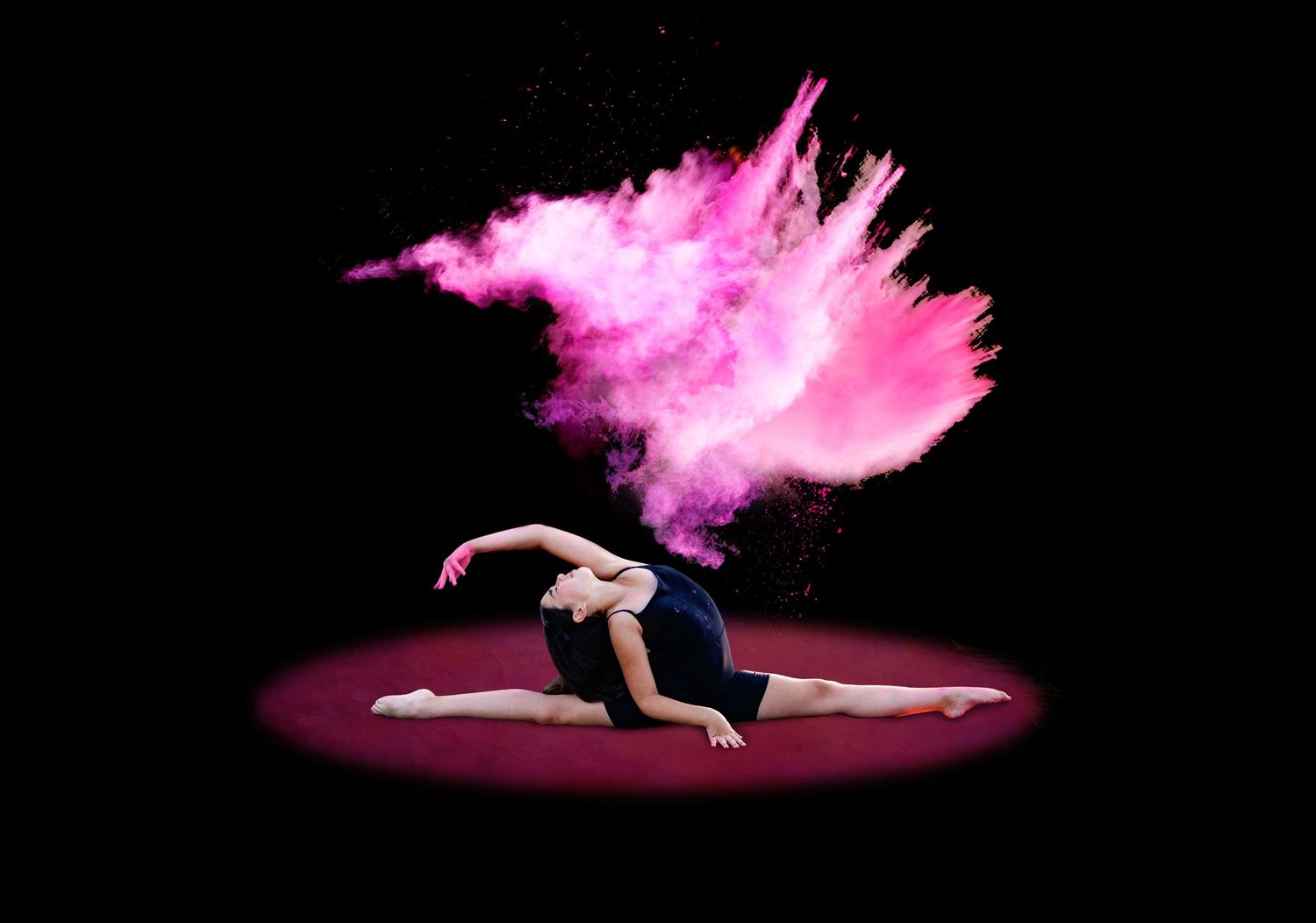 Dancer does splits on floor with dramatic pink powder explosion bursting overhead on dark stage.