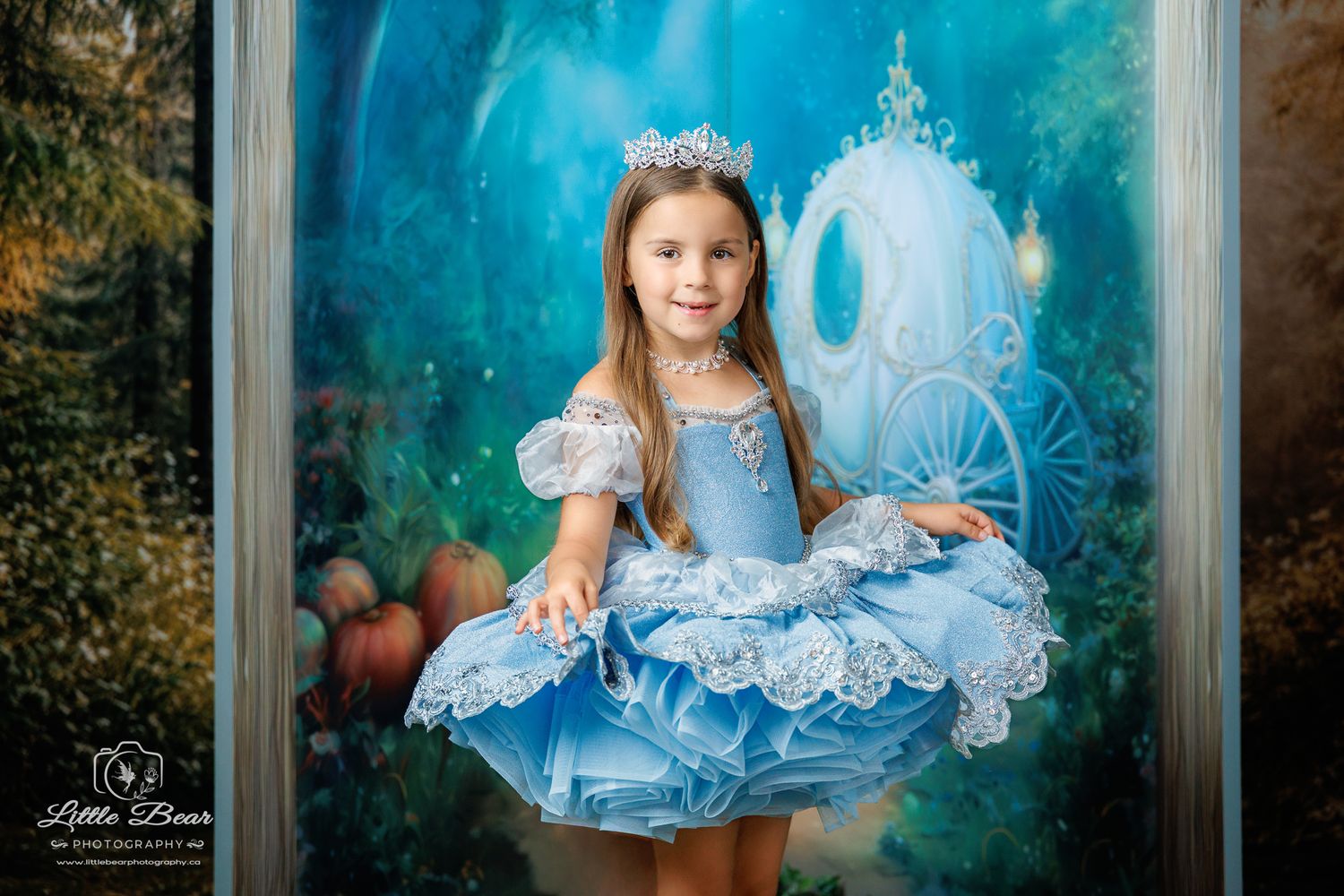 Young girl in blue Cinderella princess dress and crown poses before a magical fairytale carriage backdrop.