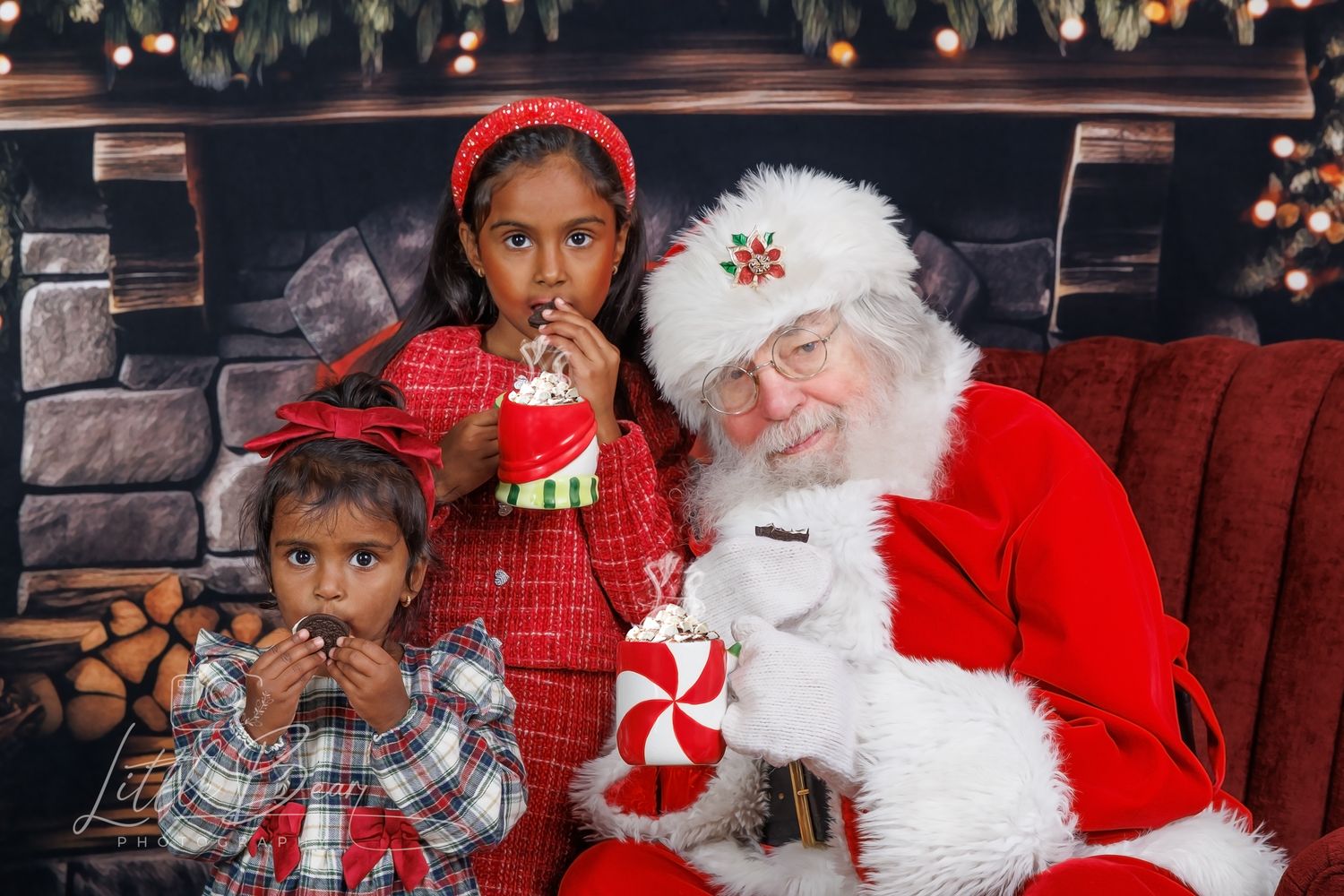 Two children sit with Santa Claus by a festive fireplace, enjoying holiday treats and candy canes.
