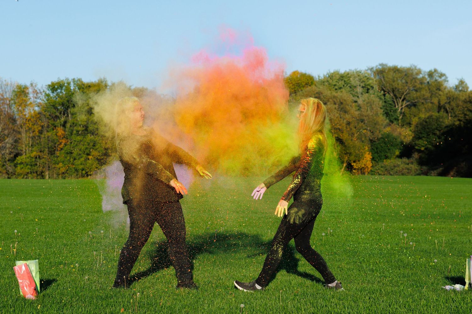 Two people throwing colorful orange and yellow powder at each other on a green field.