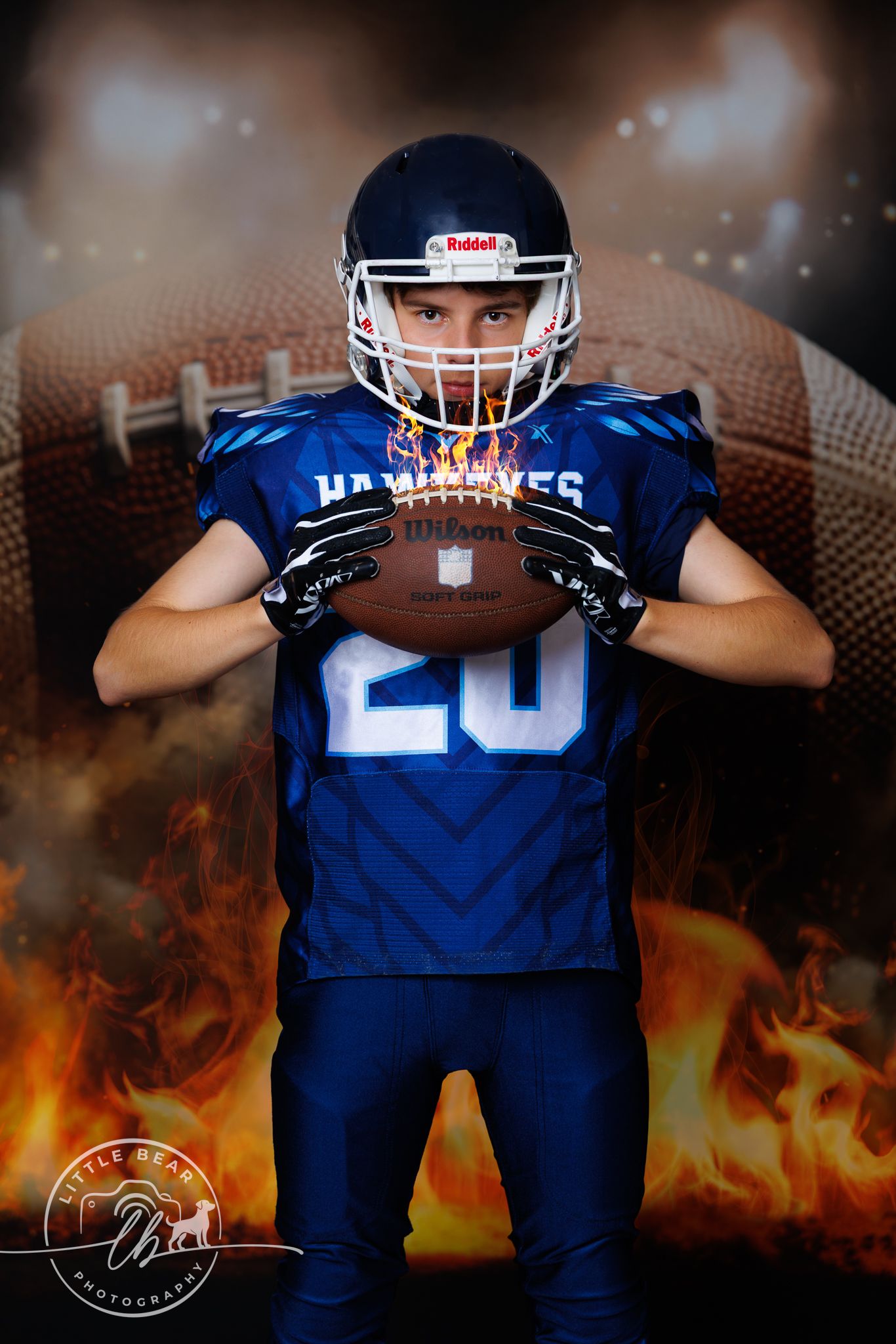Young Hawkeyes football player number 20 holding Wilson football with dramatic fire and stadium background.
