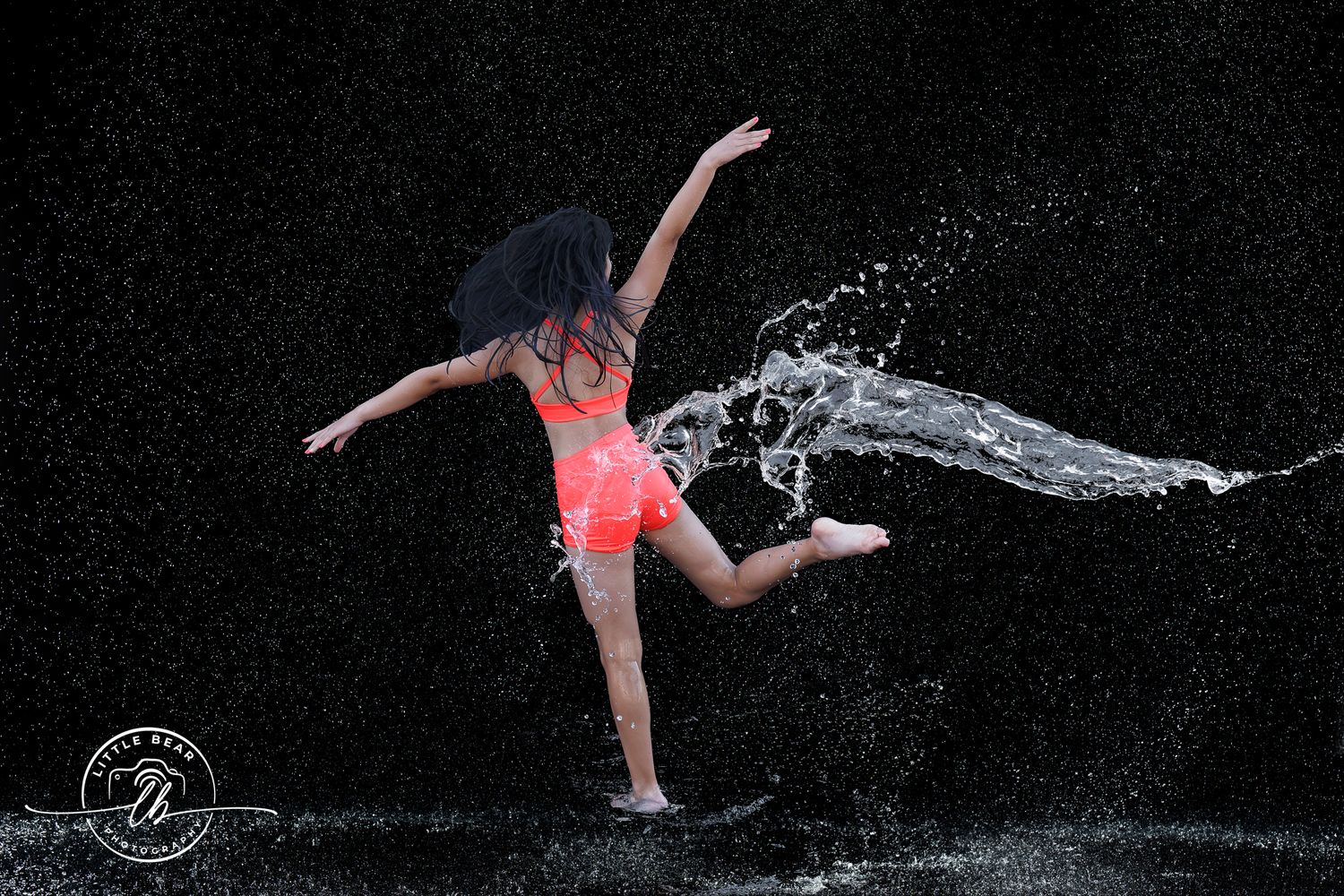 A dancer in a red outfit kicks water creating a dramatic splash against a dark background.
