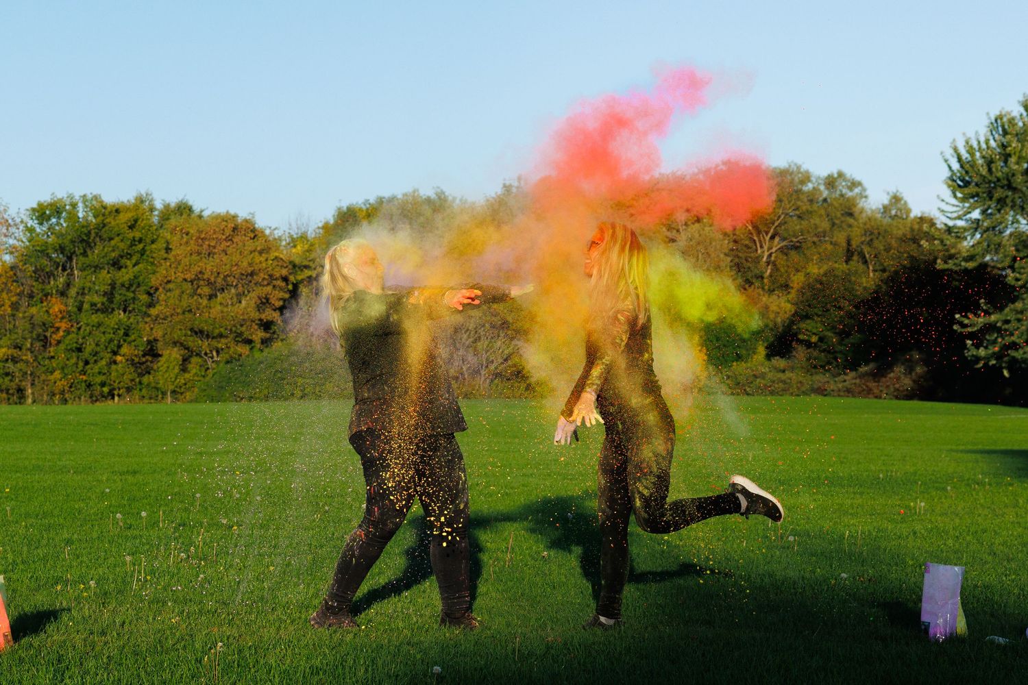 Two people covered in colorful powder running and playing on a bright green field.