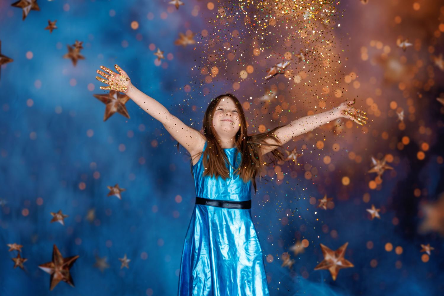 A joyful girl in a blue dress tosses gold star confetti against a sparkling blue and orange bokeh background.