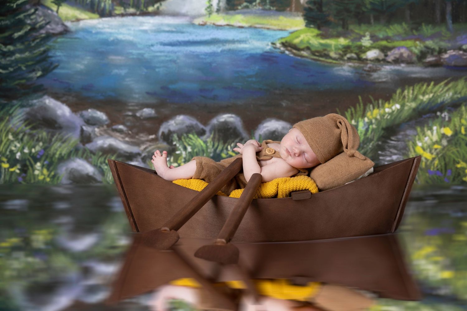 Sleeping newborn in brown bear outfit resting in boat prop against woodland stream painted backdrop.