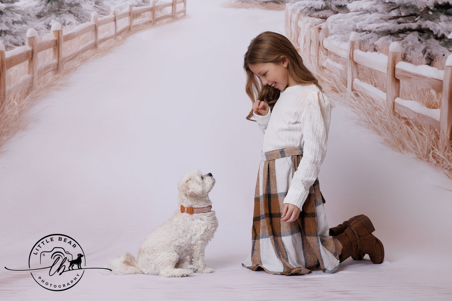 A young girl in a plaid skirt kneels beside a white fluffy dog in a snowy winter photography backdrop.