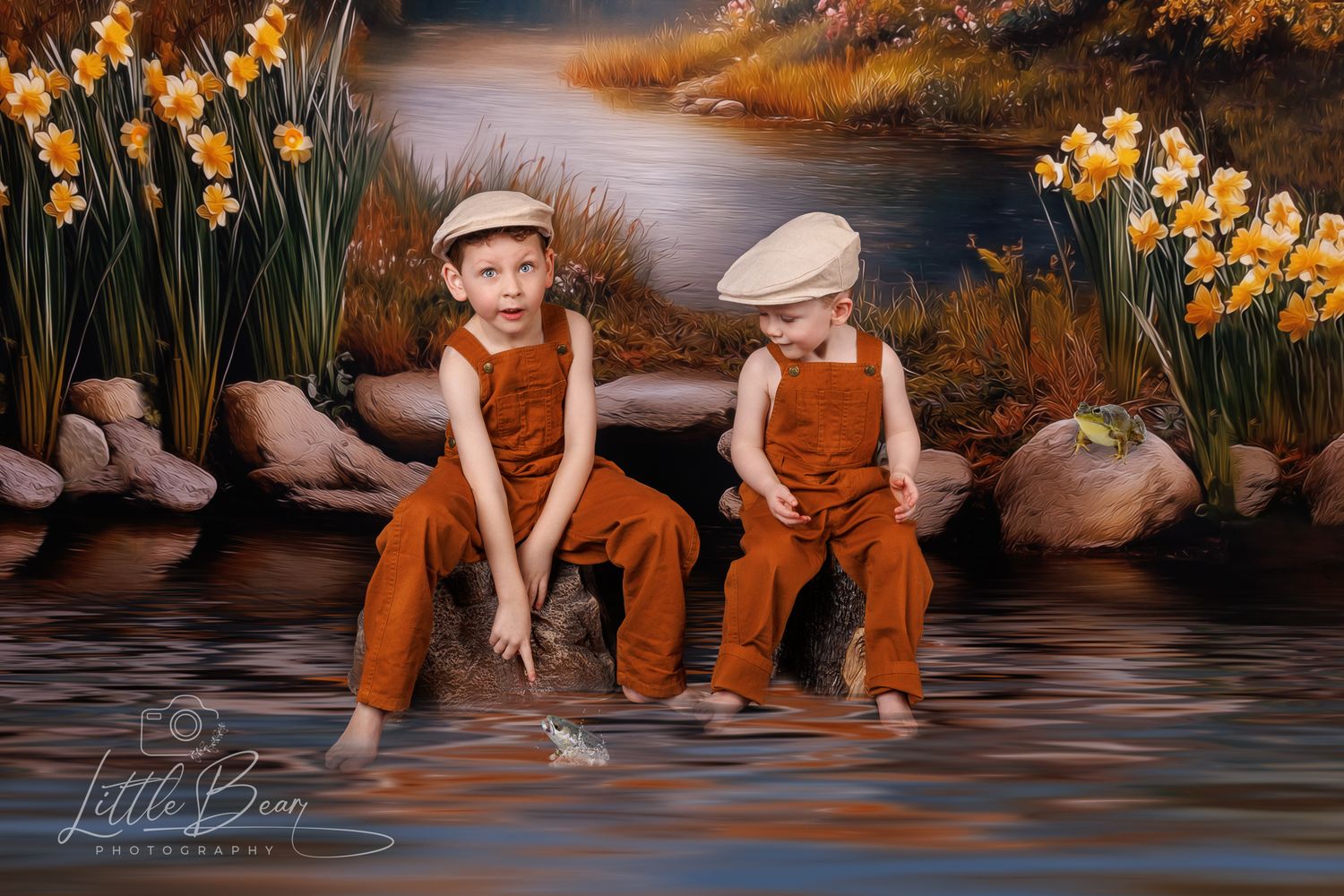 Two boys in matching brown overalls and caps sit by water with yellow daffodils in background.