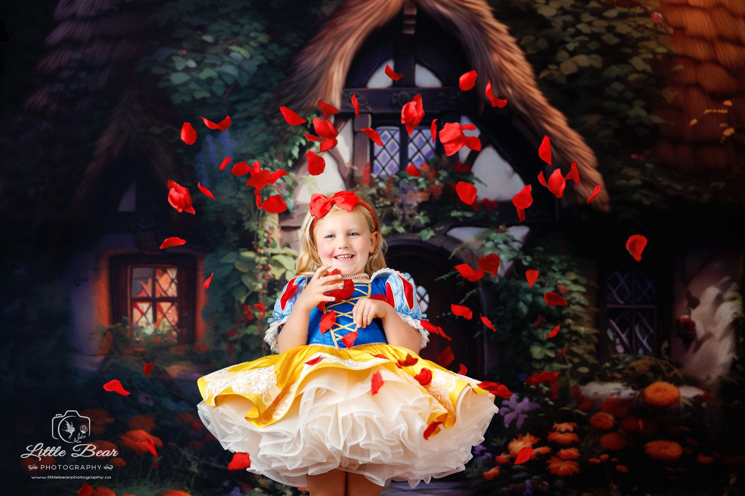 Girl in Snow White costume with red rose petals swirling around her in front of a fairy tale cottage backdrop.