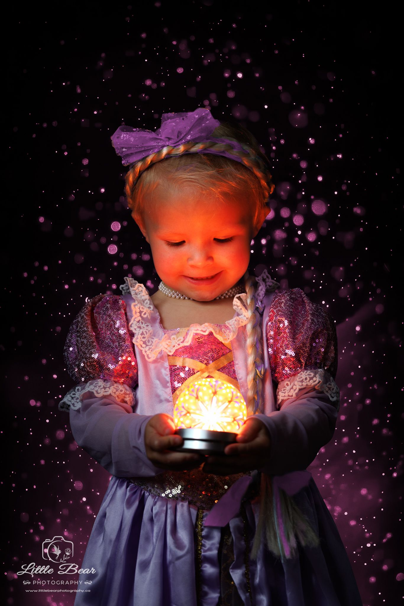 Toddler girl in Rapunzel costume holding glowing orb with purple bokeh sparkles in magical fantasy portrait.