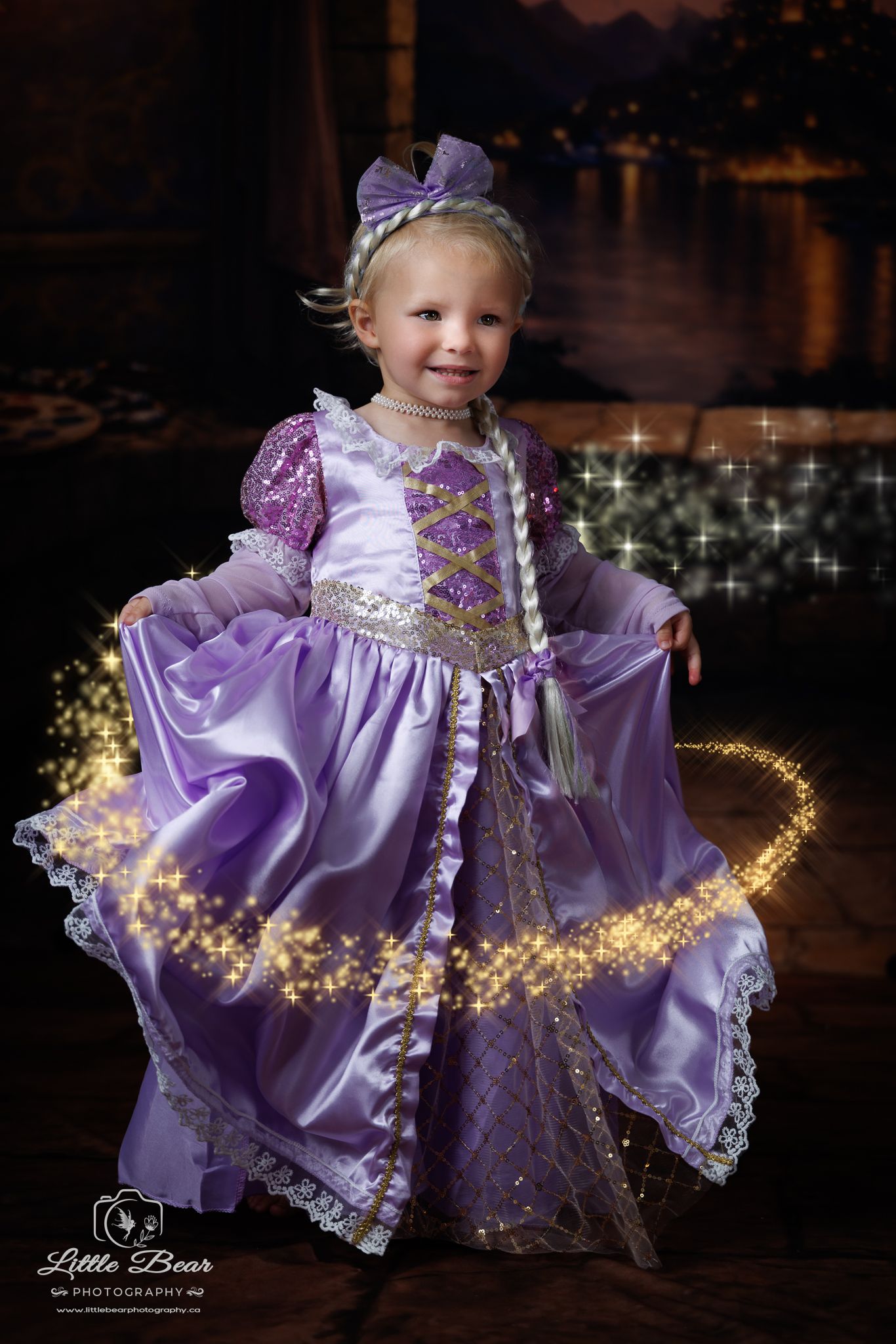 Toddler girl in purple Rapunzel princess gown with gold sparkles, smiling at Little Bear Photography studio.