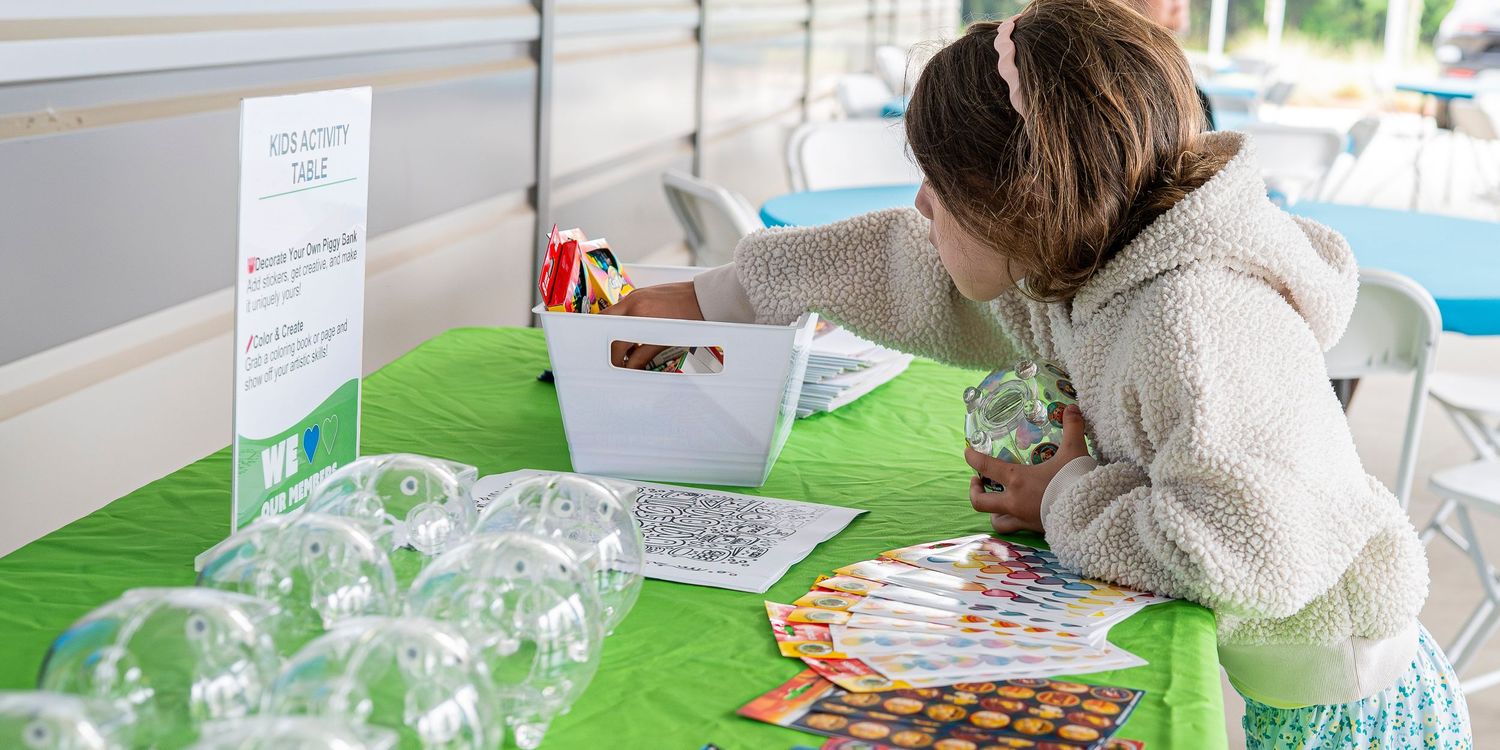 Young girl browses activity sheets at a green-covered outdoor activity table with clear ornaments displayed.