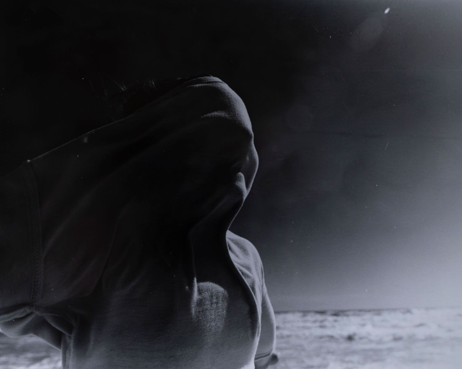 Mysterious dark silhouette of a hooded figure against a dramatic stormy sky in black and white.