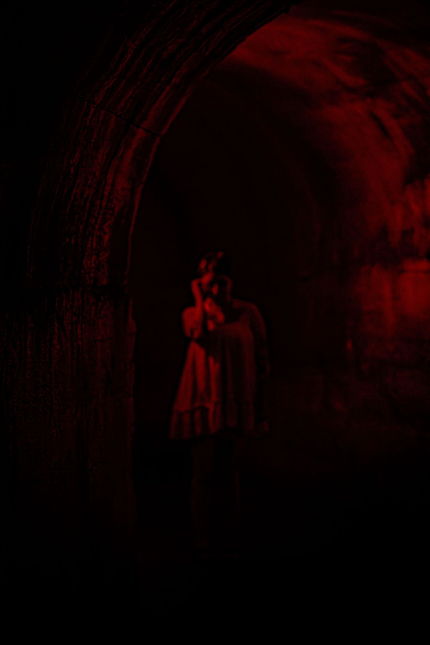Mysterious figure in white dress standing in dark tunnel illuminated by dramatic red light.