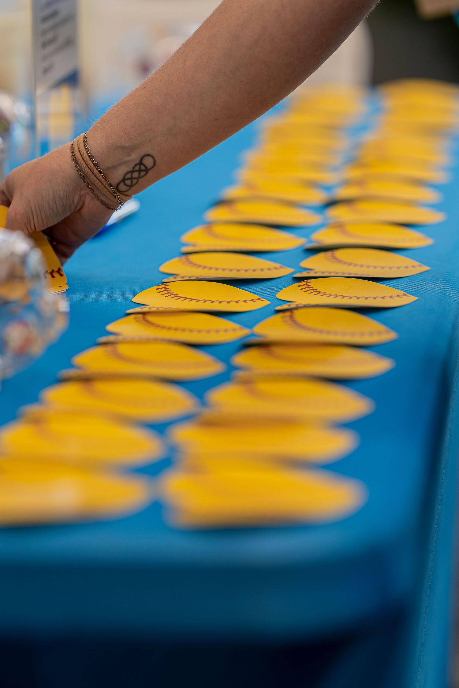 Hand reaching for yellow softball-shaped keychains arranged on a blue tablecloth.