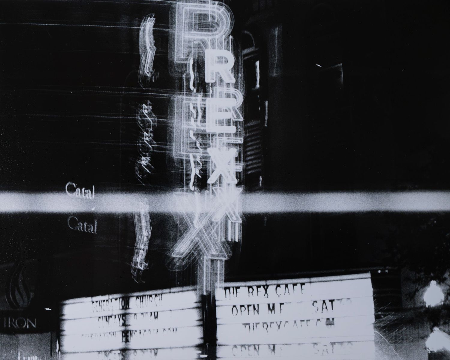 Blurred black and white long exposure photo of REX cafe neon sign at night.