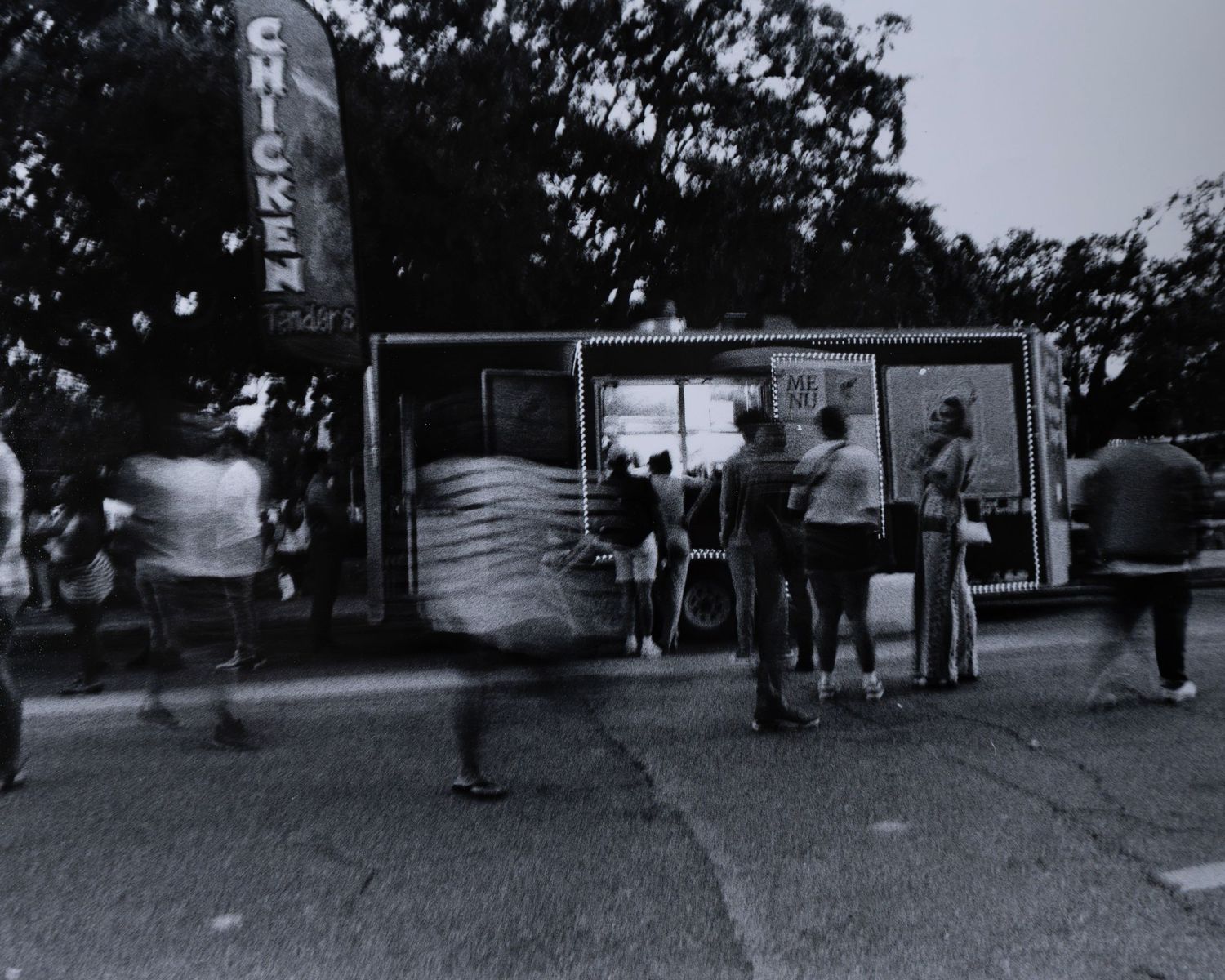 Black and white photo of people at outdoor chicken food stand with motion blur.