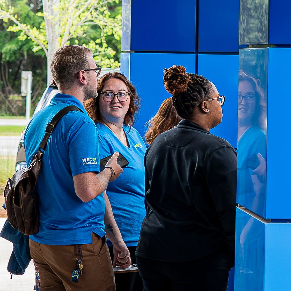 Credit union staff in blue shirts greeting members outside a modern blue building.