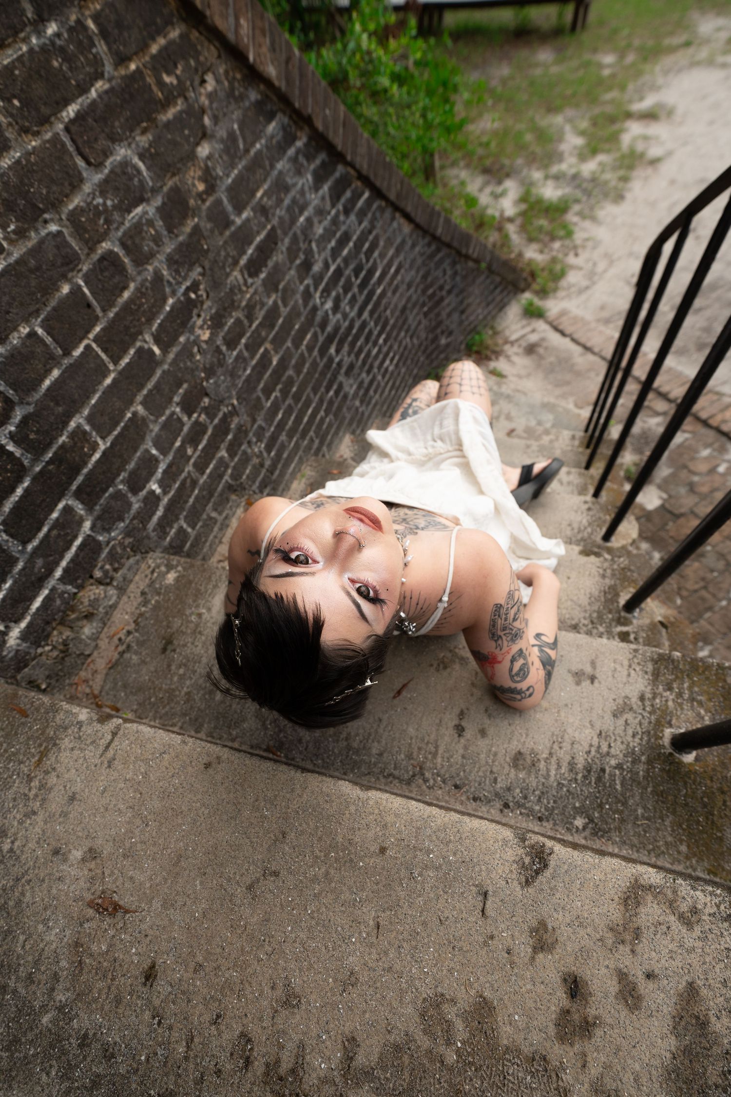 Aerial view of tattooed woman in white dress lying on outdoor concrete steps, black and white photo.