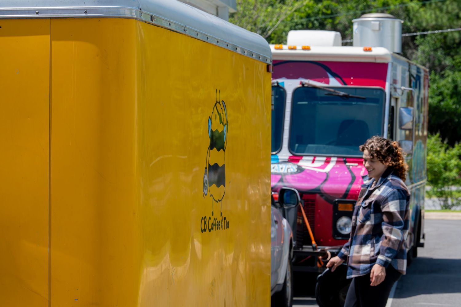 Woman standing between colorful yellow and pink food trucks at an outdoor event.