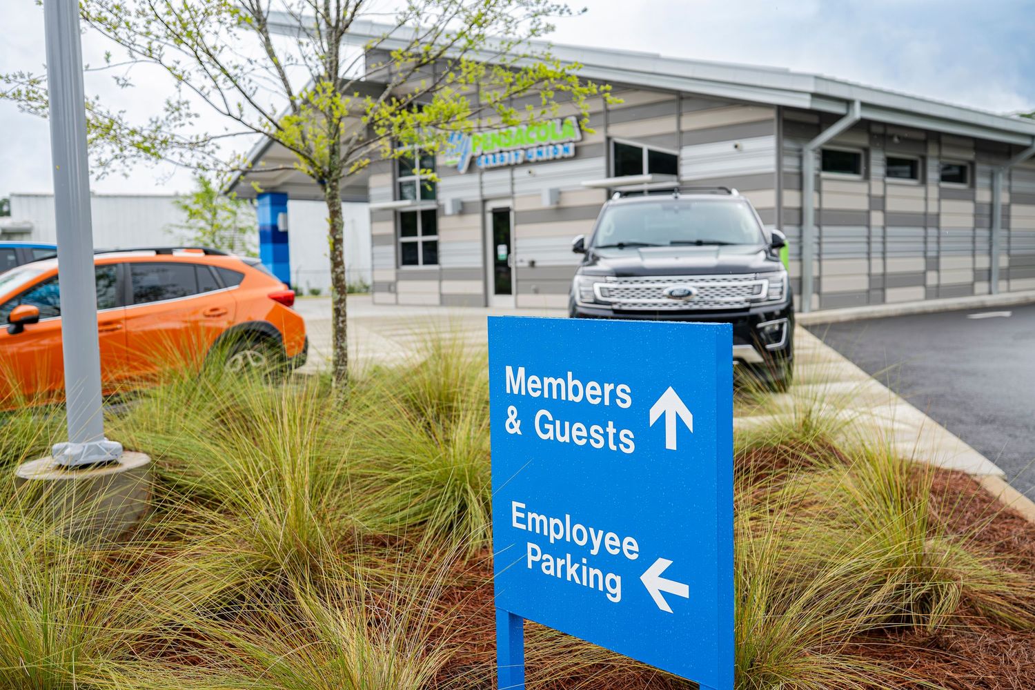 Blue directional sign for members, guests, and employee parking outside a modern credit union branch.