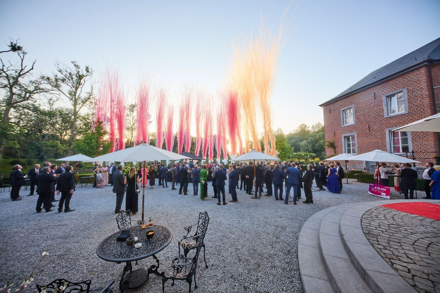 Outdoor event venue at dusk with red flags lining the walkway and guests gathering.