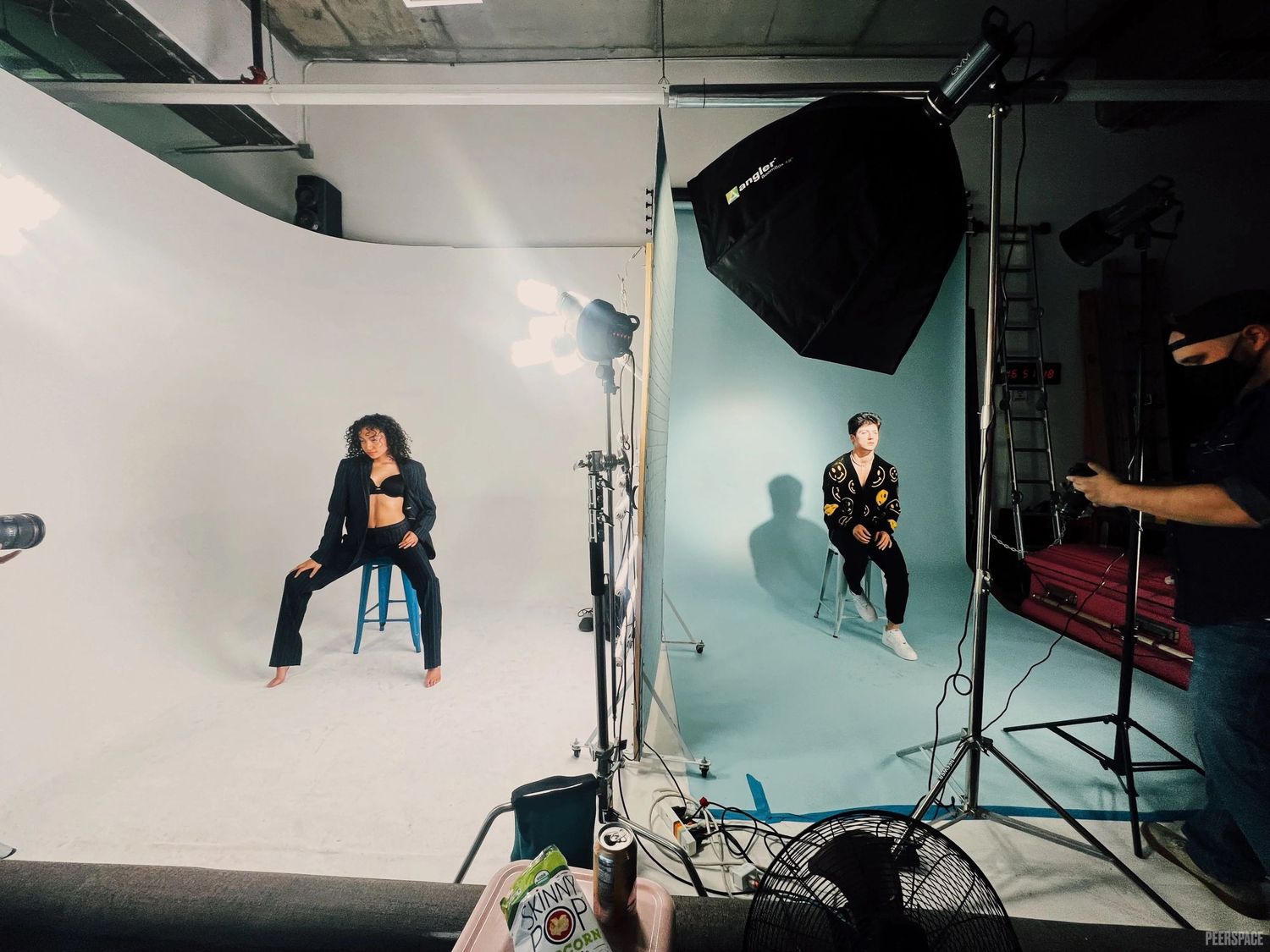 Two individuals sit on stools on a cyc wall. Specialty photography lighting illuminates them. One half of the cyc is white, the other blue.