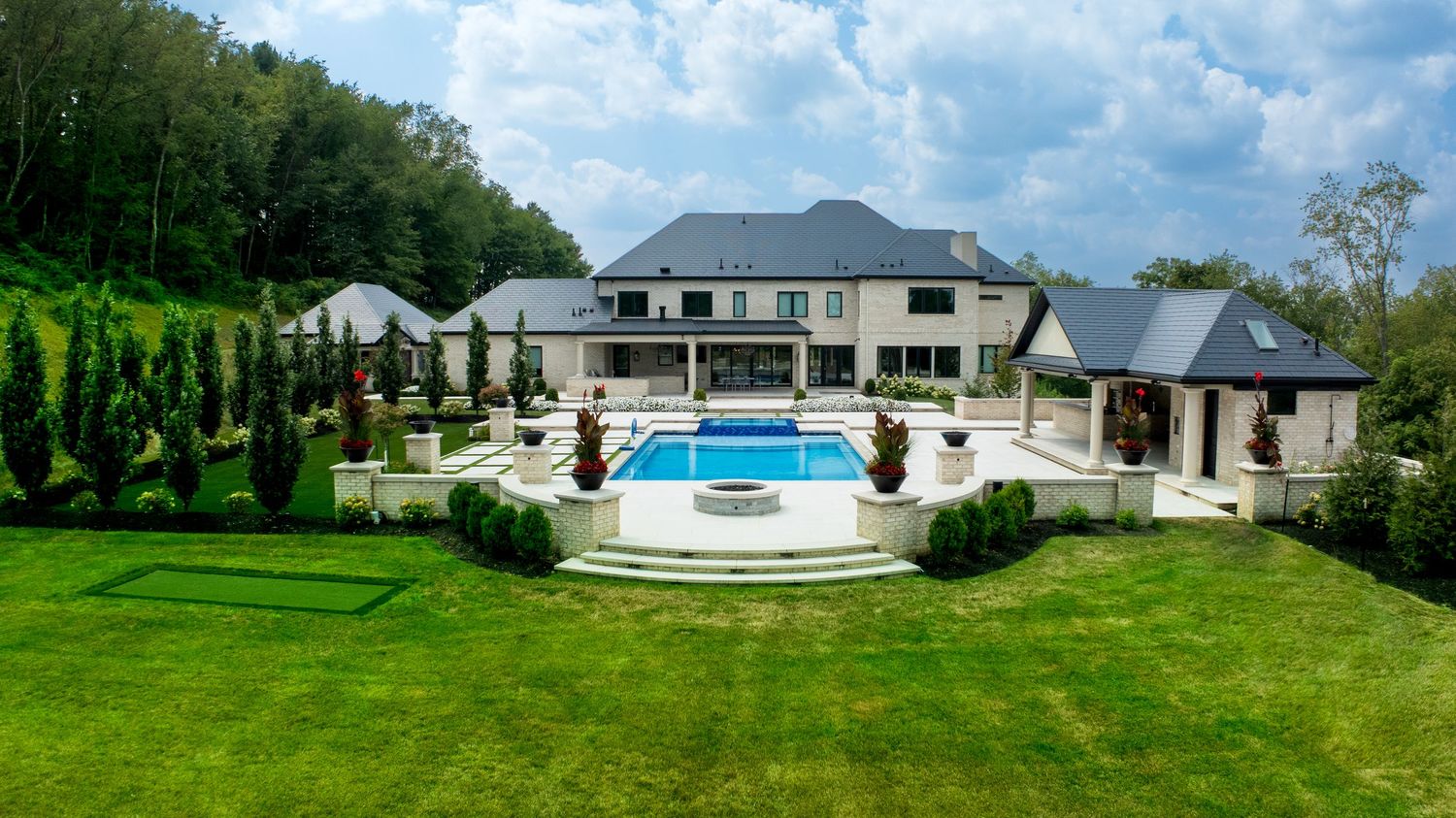 Elevated view of a residence, swimming pool, pool house, and landscaped lawn.