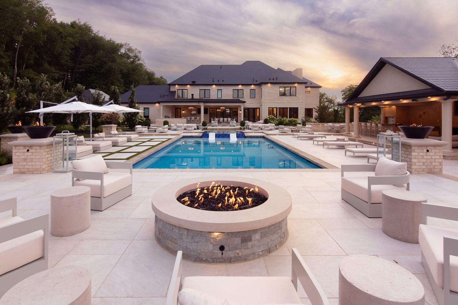 Pool courtyard and fire pit at sunset with a residence and pool house beyond.