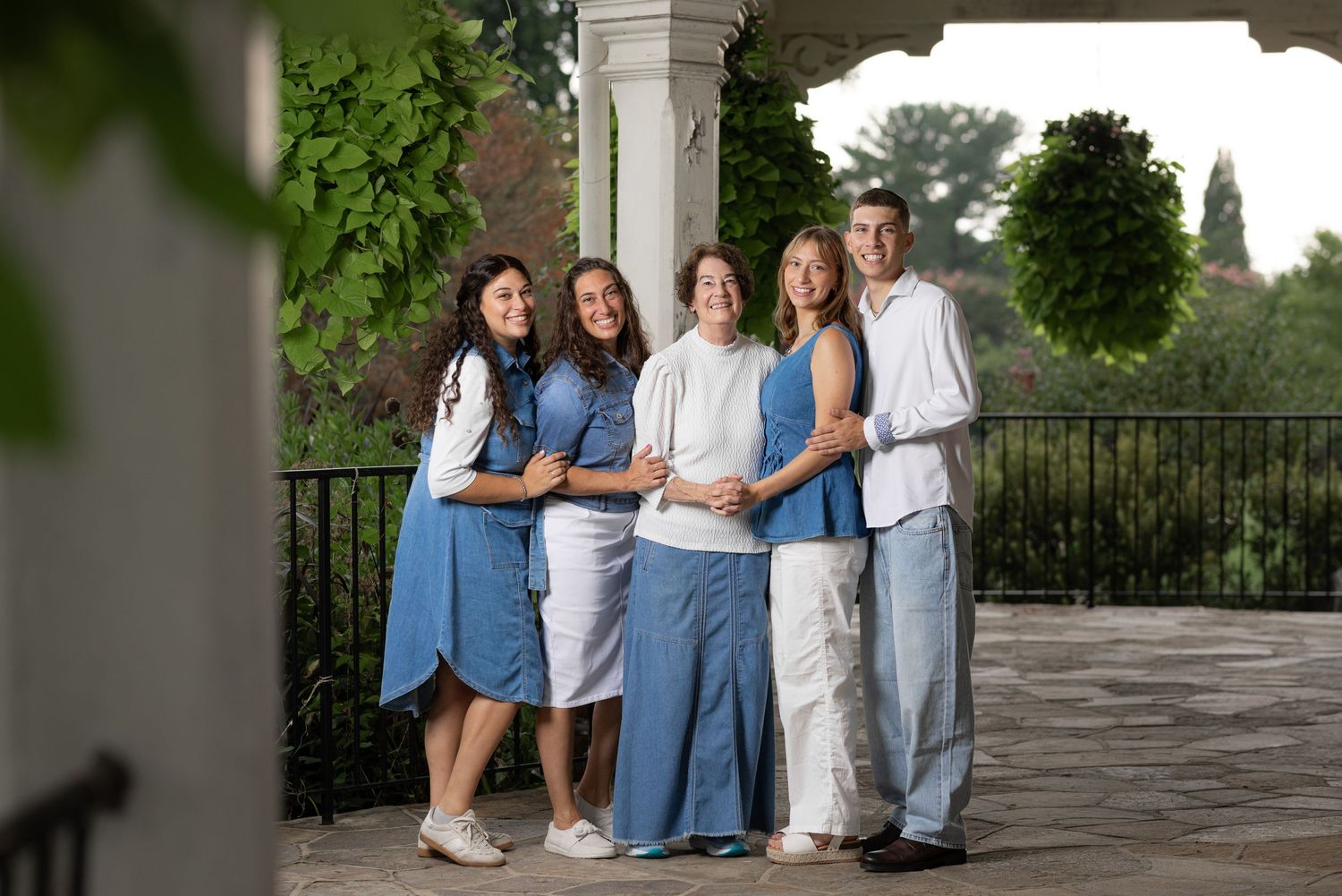 Family of five posing together under a columned porch, wearing coordinated blue and white outfits outdoors.