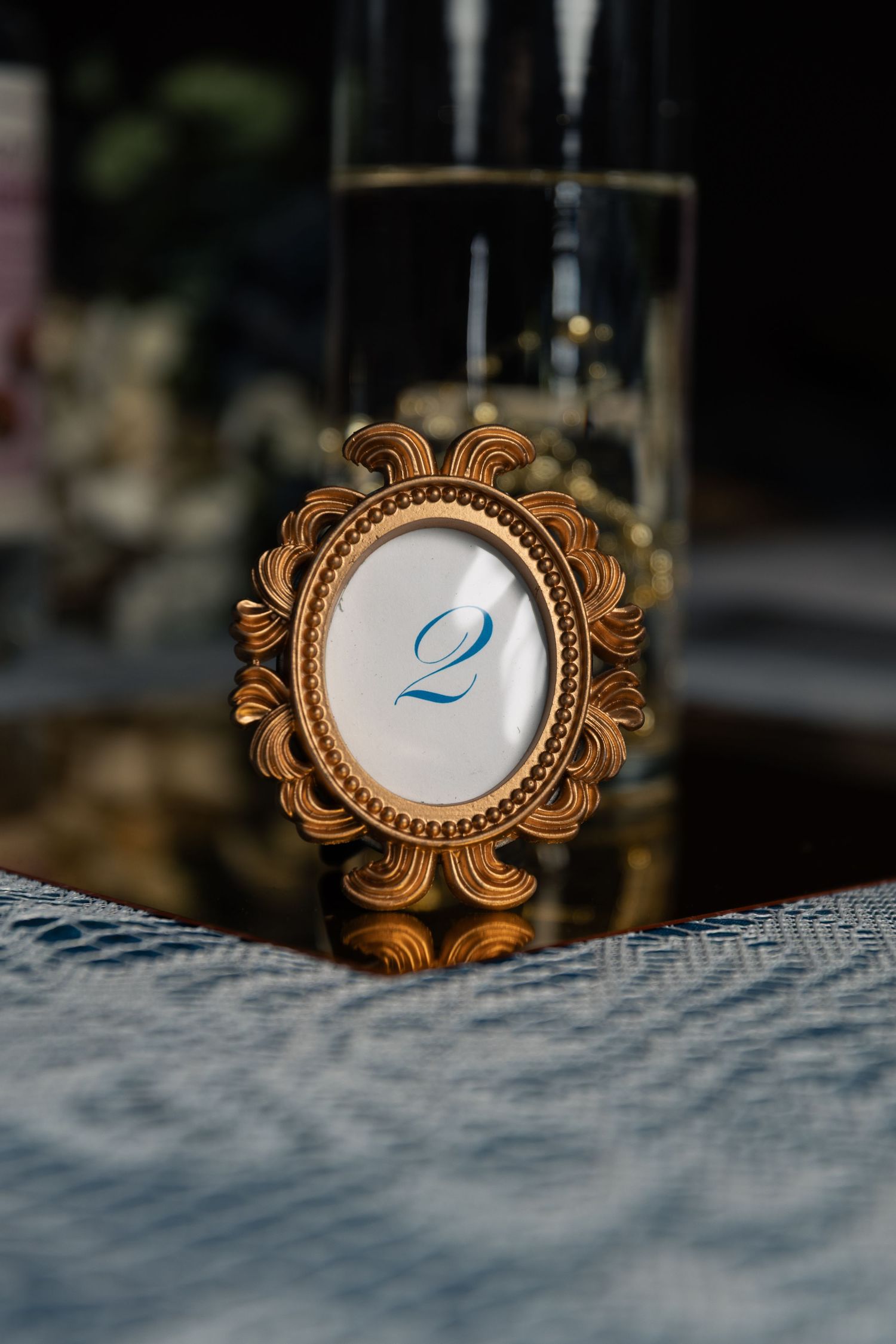 Ornate gold oval picture frame displaying table number two at an elegant wedding reception.