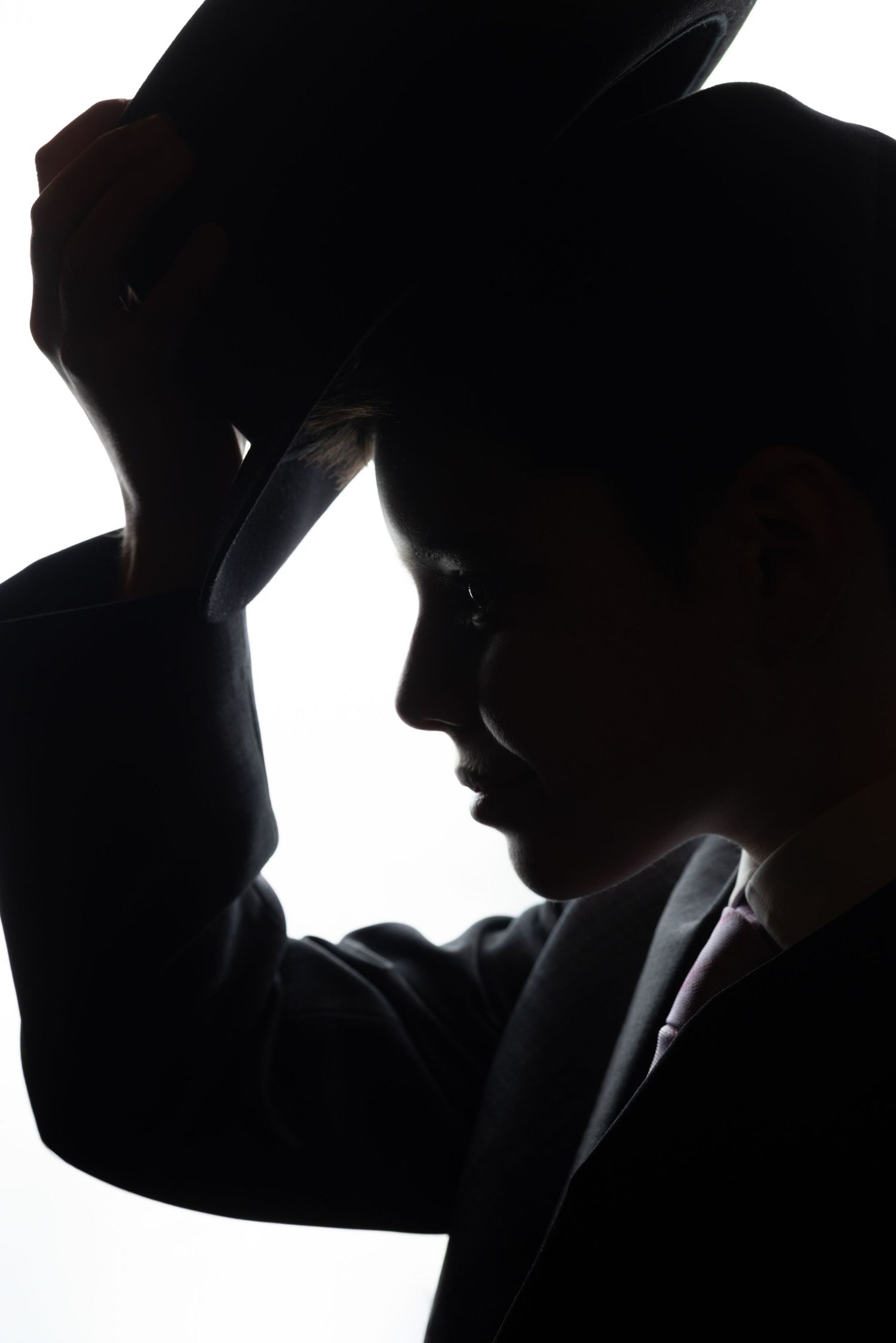 A dramatic silhouette of a young boy in a suit tipping his fedora hat against a bright background.