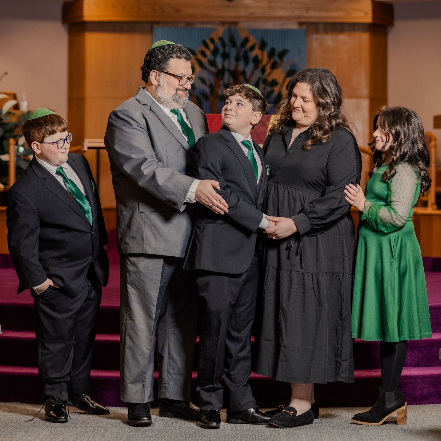 Family of five sharing a warm moment together in a church, dressed in formal green and black attire.
