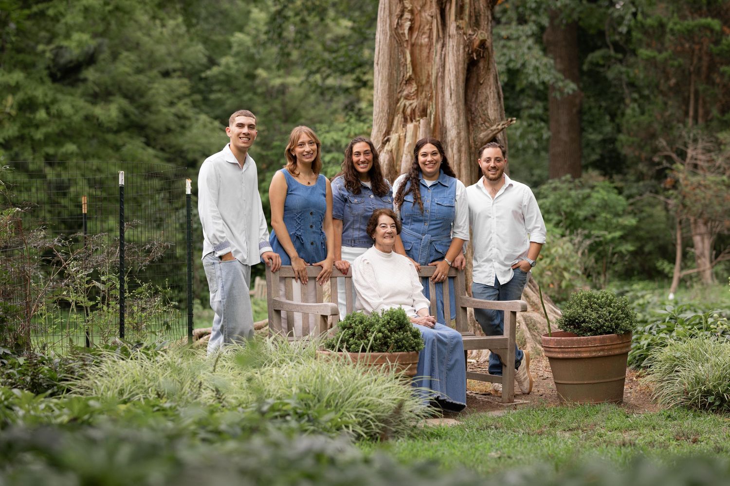 Family of six poses in a lush garden setting with towering redwood trees in the background.