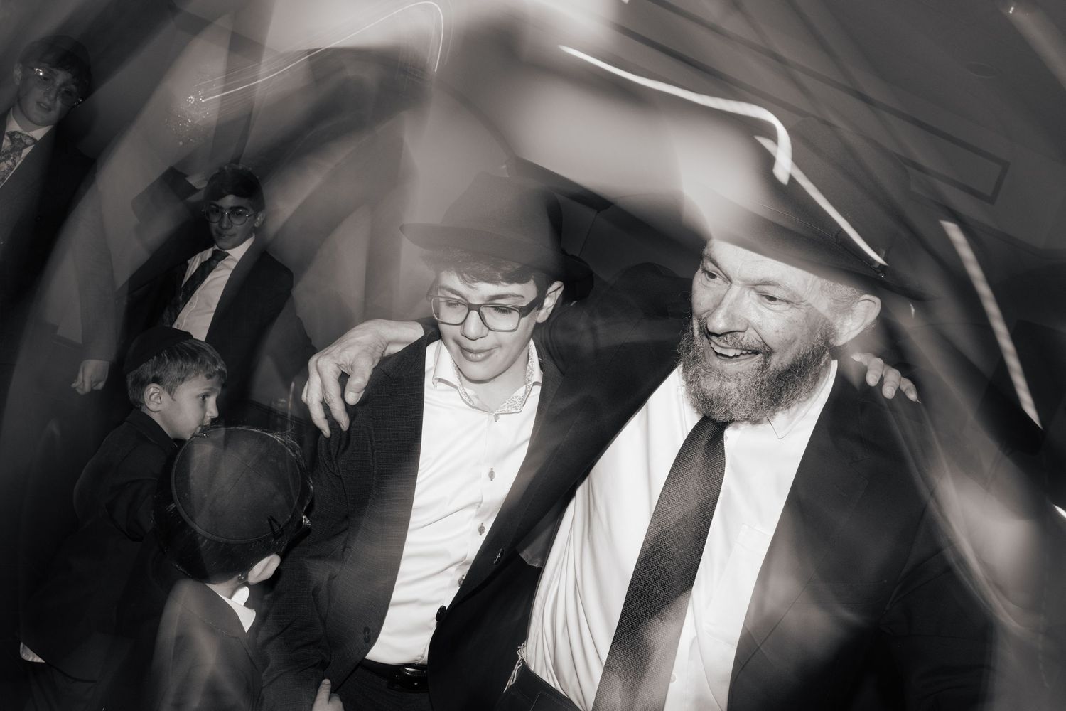 Boy in glasses celebrates with bearded man at joyful Bar Mitzvah party in black and white.