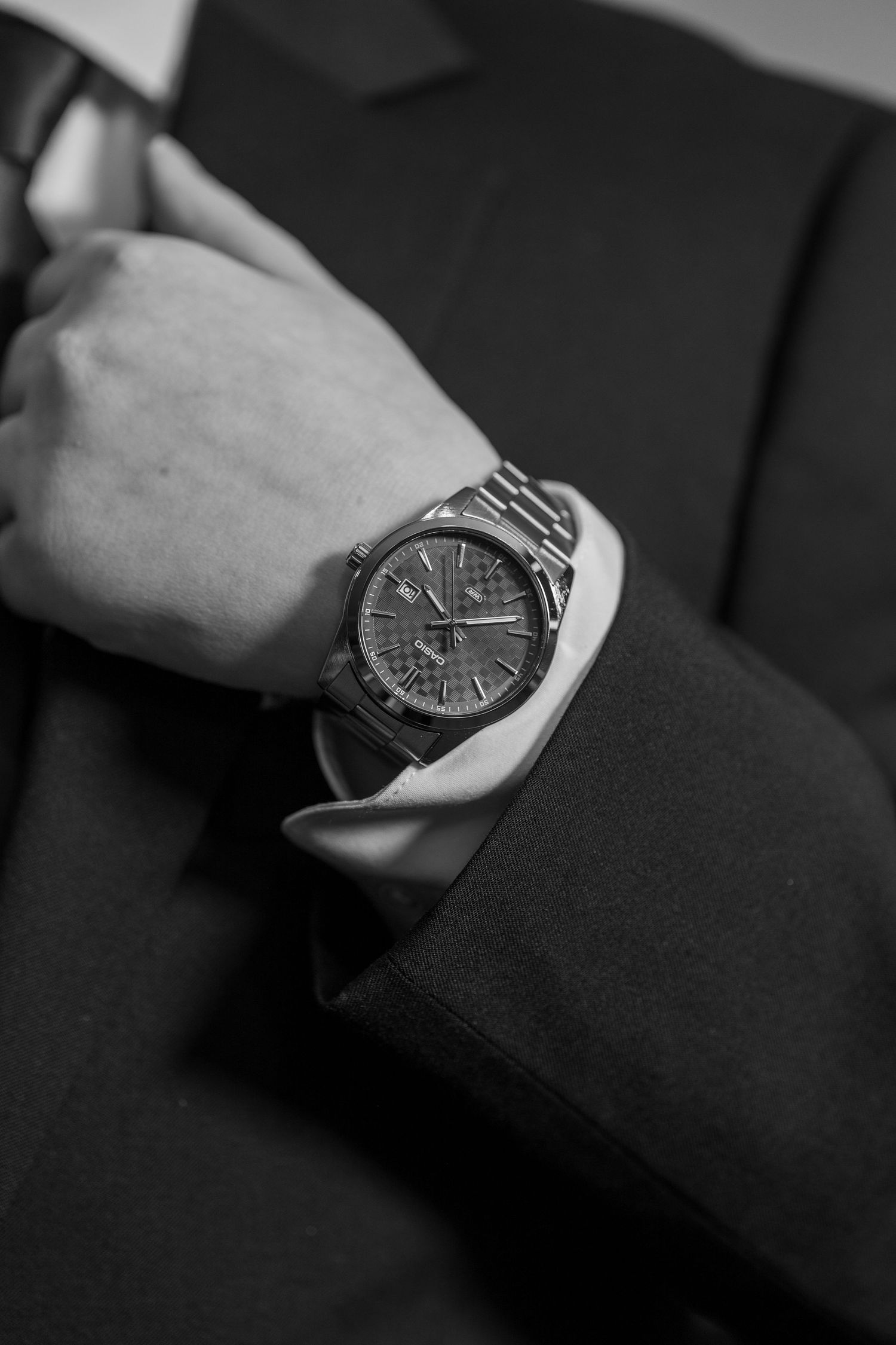 Close-up black and white photo of a luxury chronograph wristwatch on a mans wrist in a suit.
