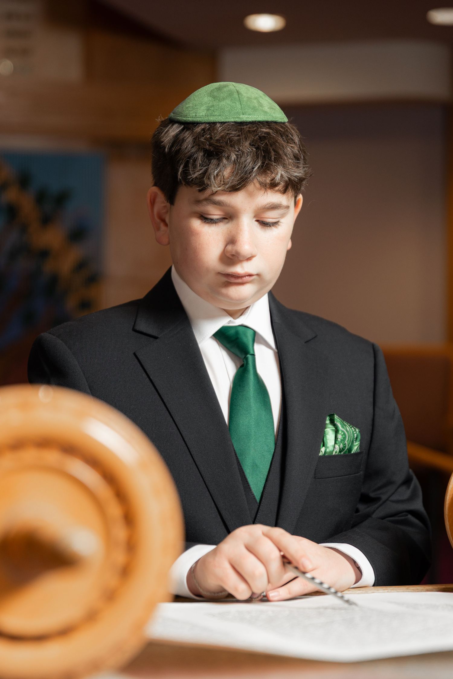 A young boy in a black suit and green yarmulke reads from the Torah at his Bar Mitzvah.