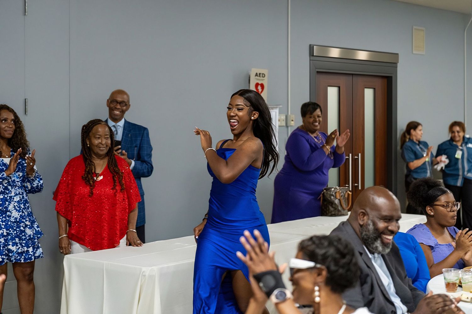 Joyful celebration event with guests in blue and red attire dancing and clapping in a decorated banquet hall.