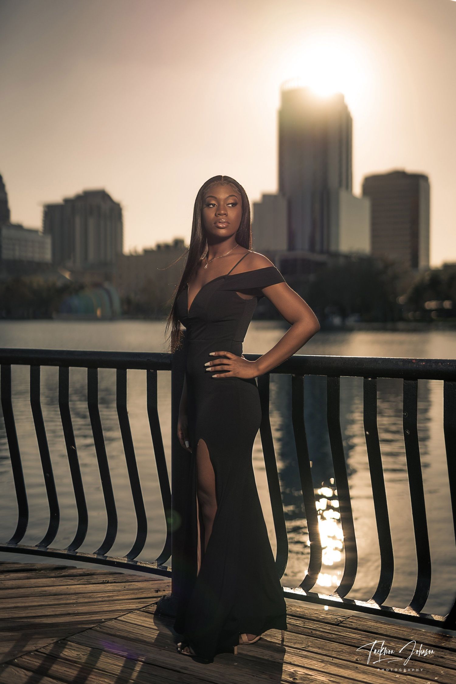 Silhouetted figure poses against sunset skyline on waterfront boardwalk.