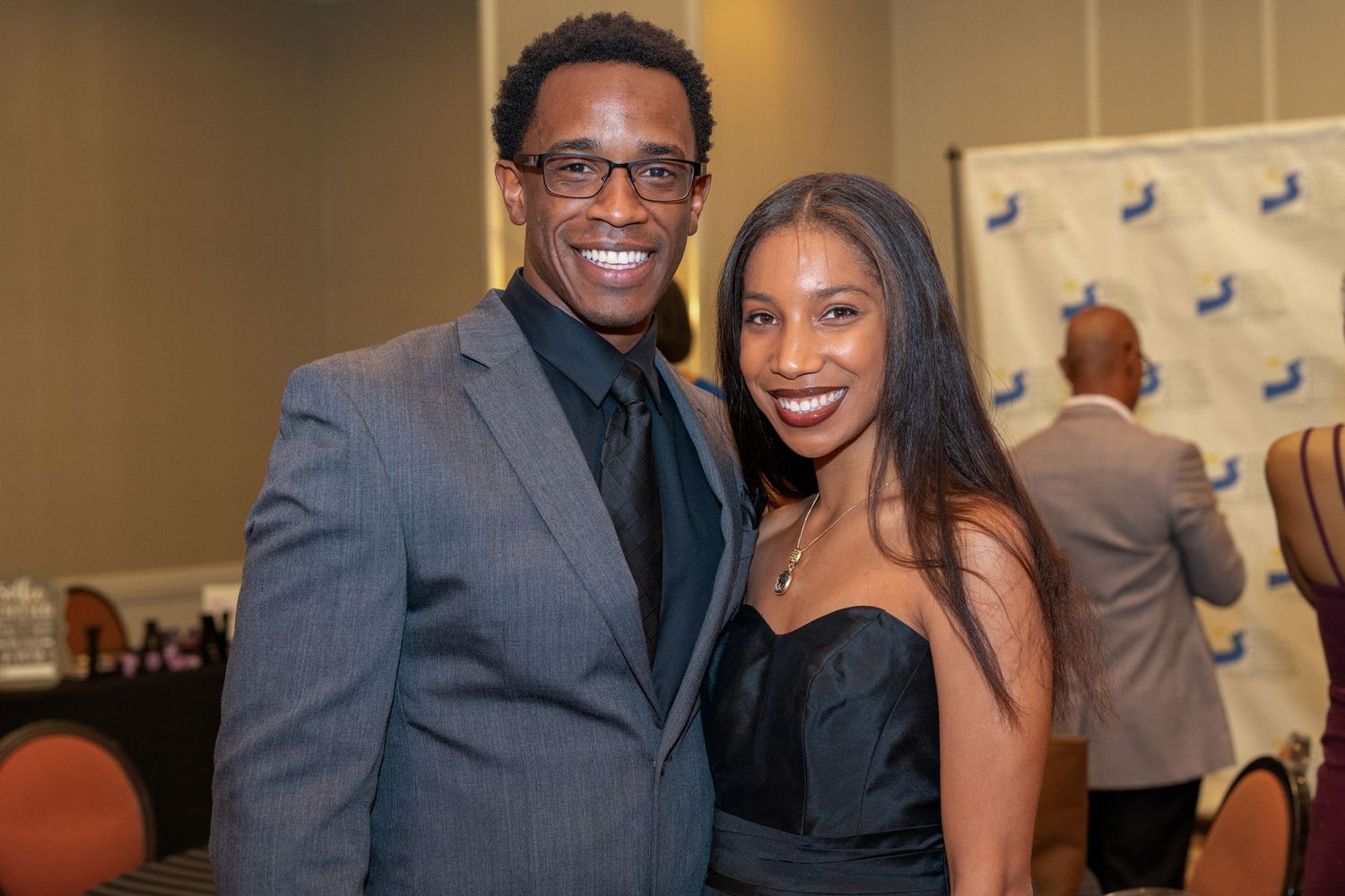 A smiling couple dressed in formal attire poses together at an elegant event venue.