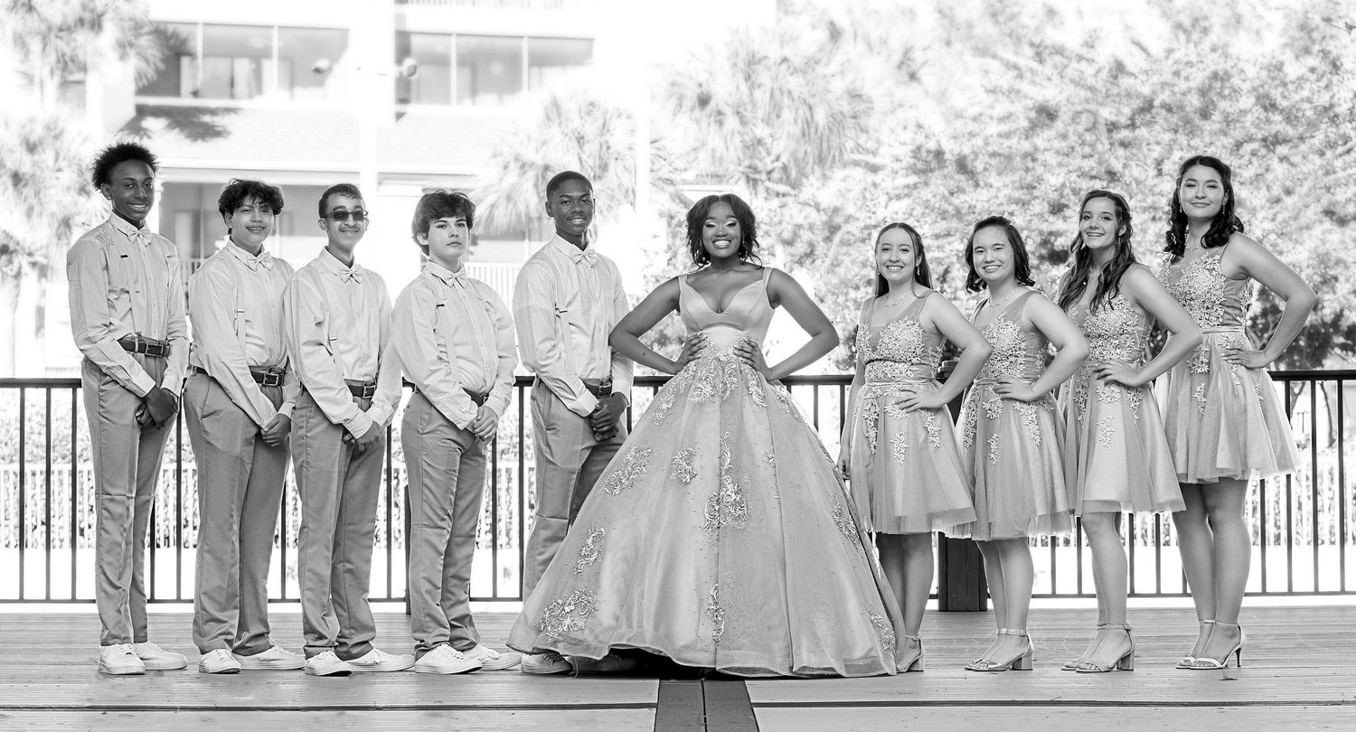 A black and white wedding party photo with bridesmaids and groomsmen flanking the central figure.