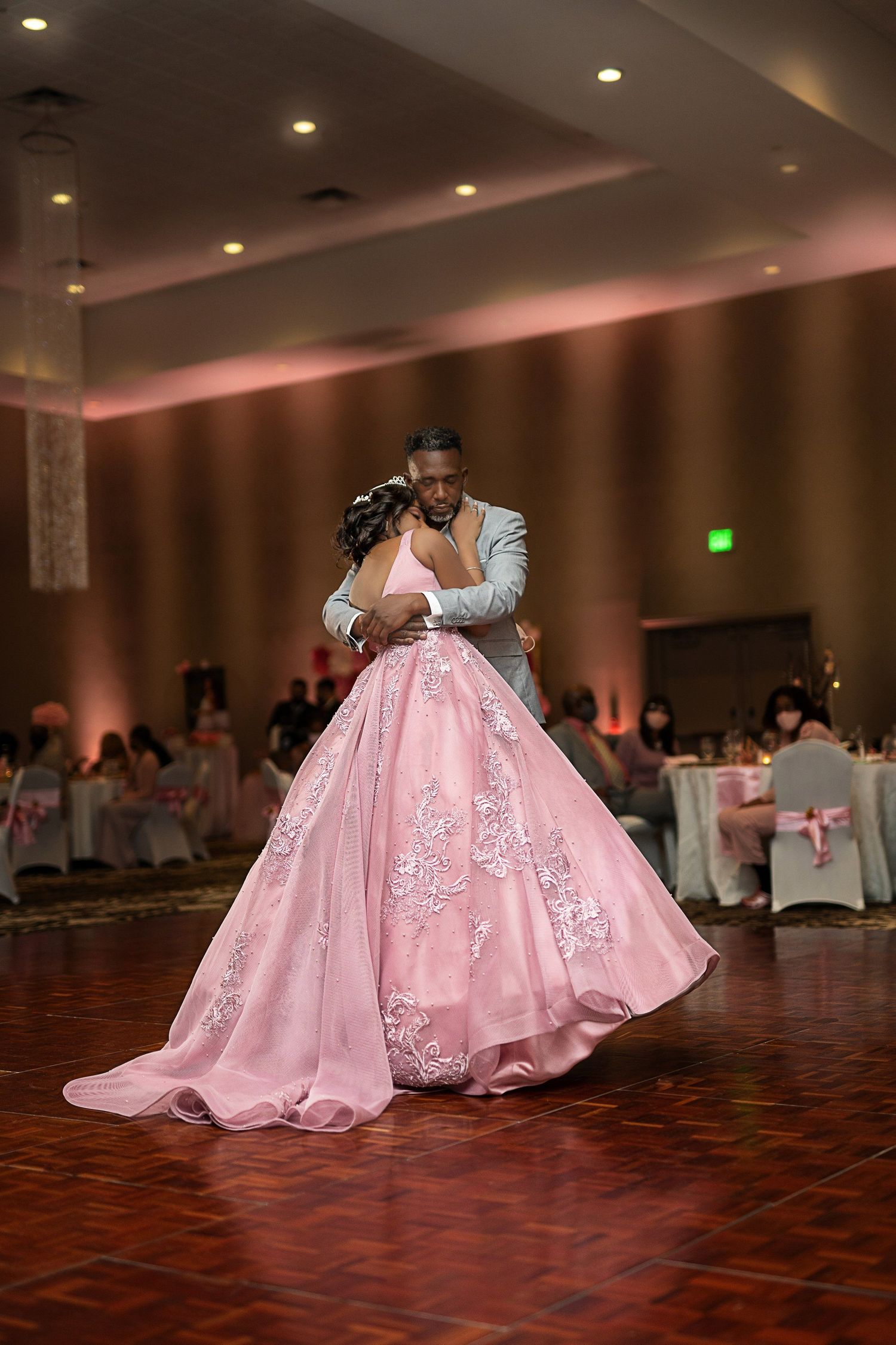 A flowing pink ballgown swirls across a polished dance floor during a formal event.