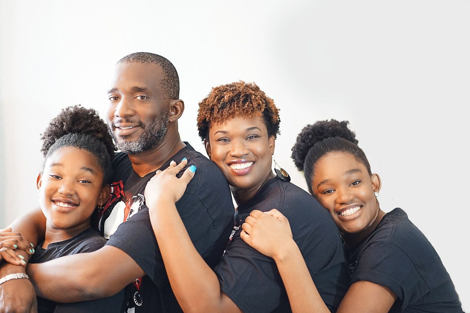 Family of four wearing black shirts posing together against white background.