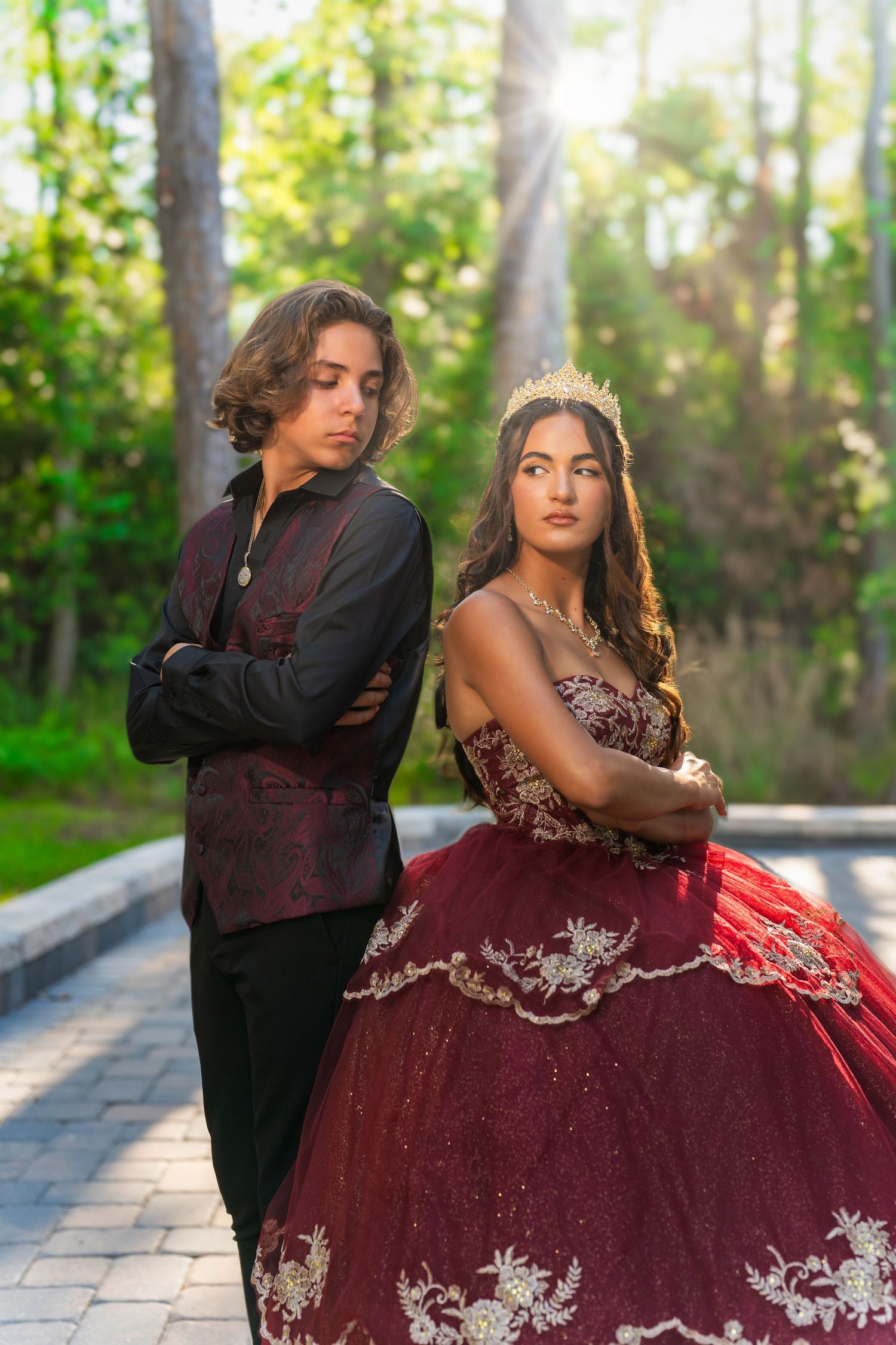 A dramatic portrait of two people in formal wear posing back-to-back on a garden path.