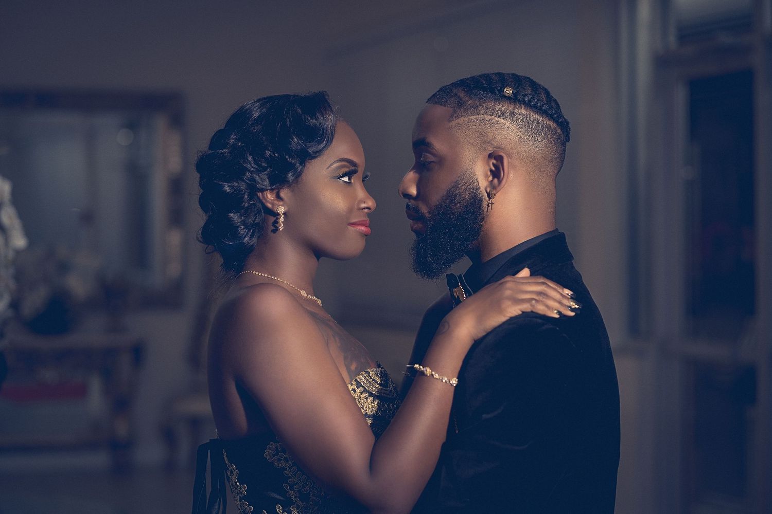 An elegant Black couple shares a romantic moment, dressed in formal attire at a wedding reception.