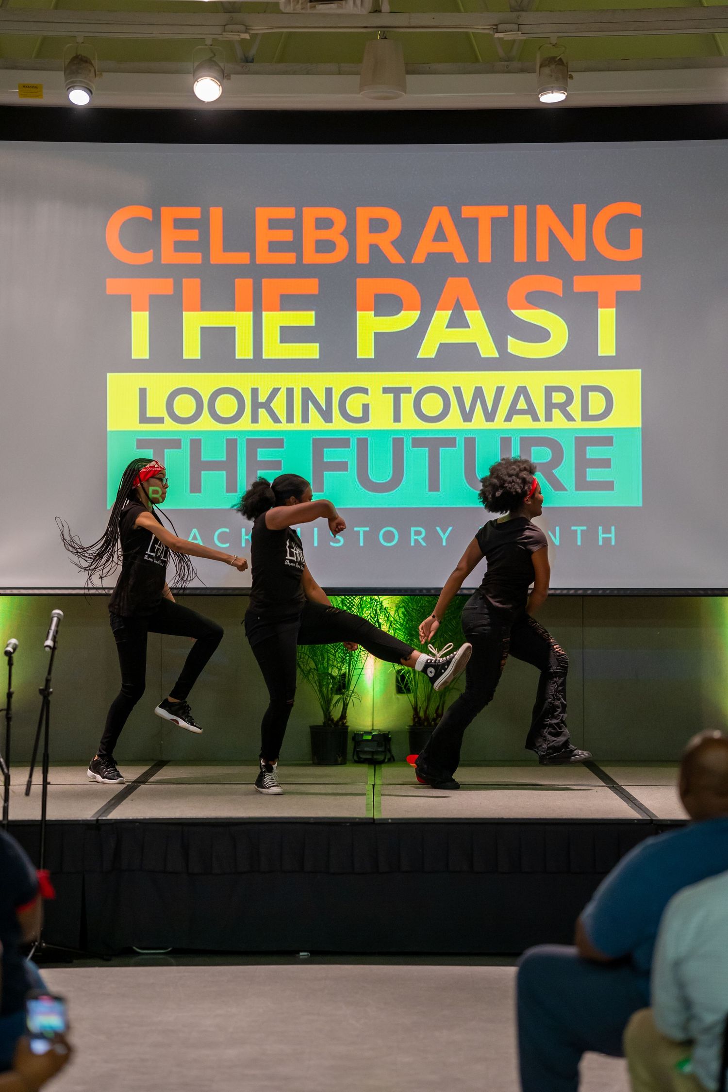 Three dancers perform on stage at a Black History Month event with colorful backdrop reading Celebrating the Past Looking Toward the Future.
