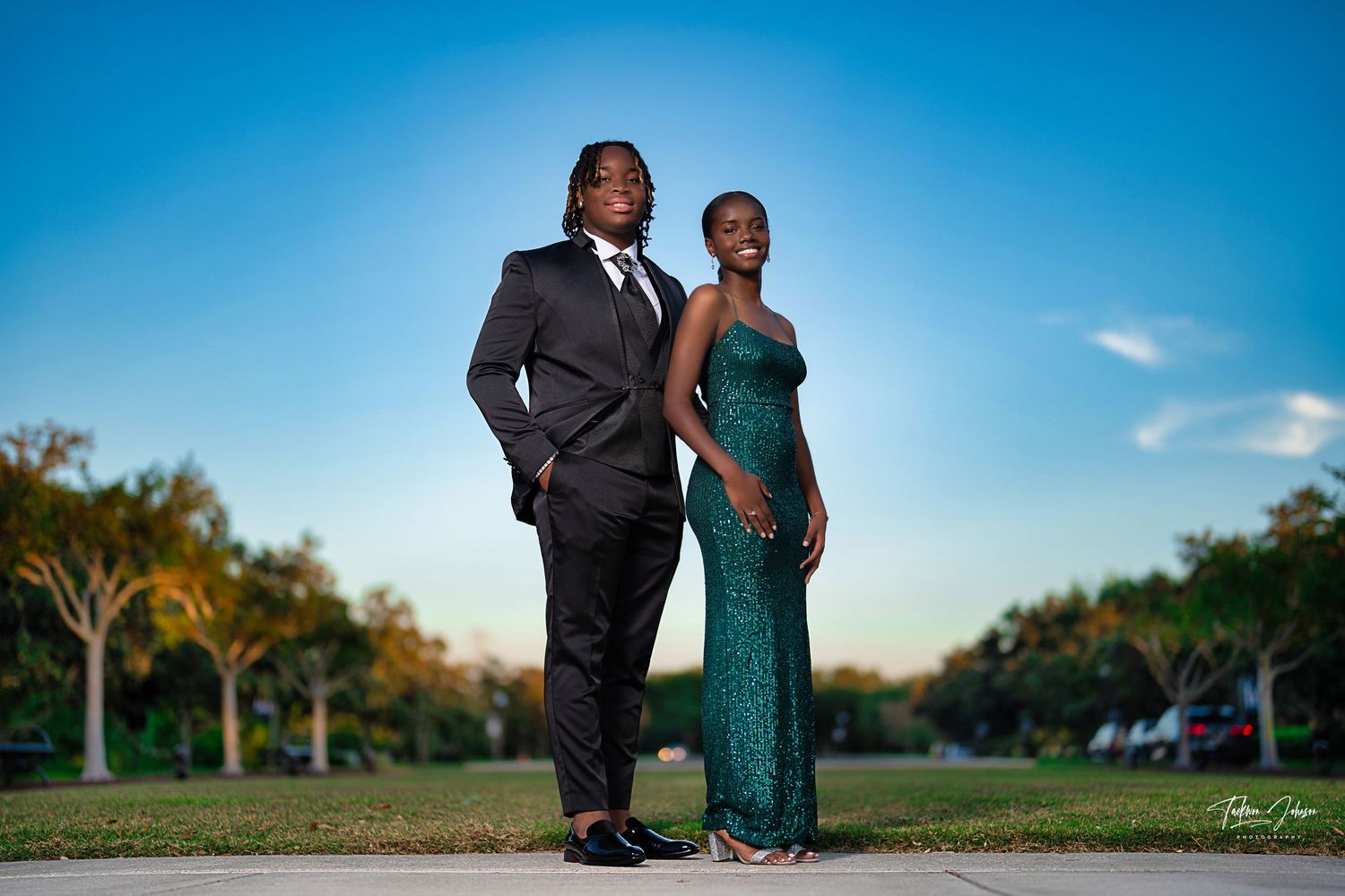 Formal couple's portrait session in park setting under bright blue sky.