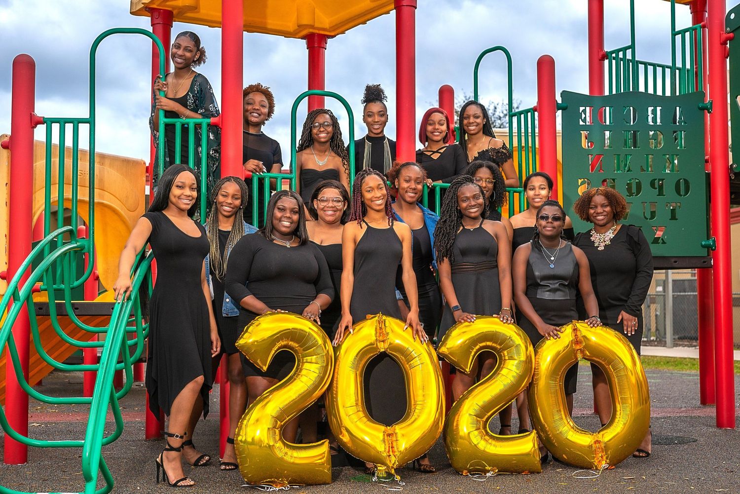 Large group of people gathered at a colorful playground with 2020 gold balloon numbers.