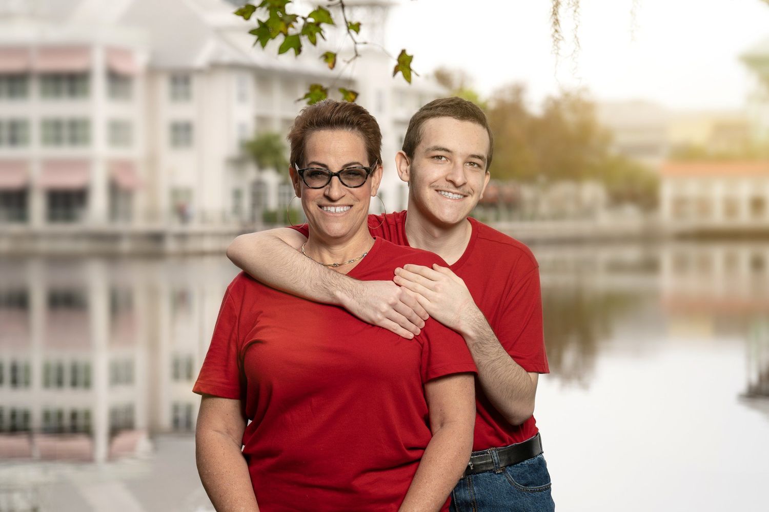 Couple in matching red shirts embracing by waterfront at sunset.